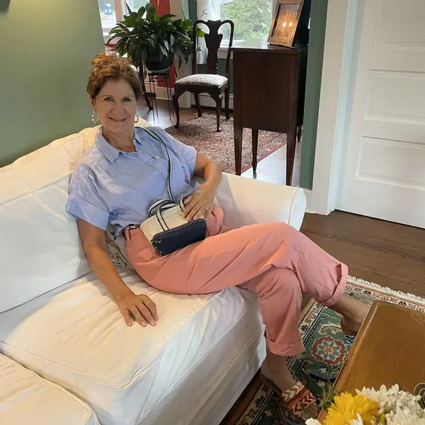 Lisa relaxing at home on a white couch in a blue shirt and pink pants