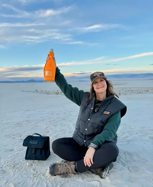 Lisa sitting on the dunes at White Sands, New Mexico, raising a drink